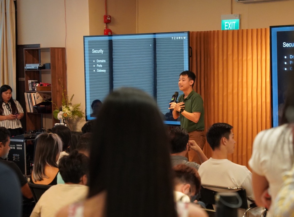 Speaker discussing security beside presentation screens with an audience in the foreground