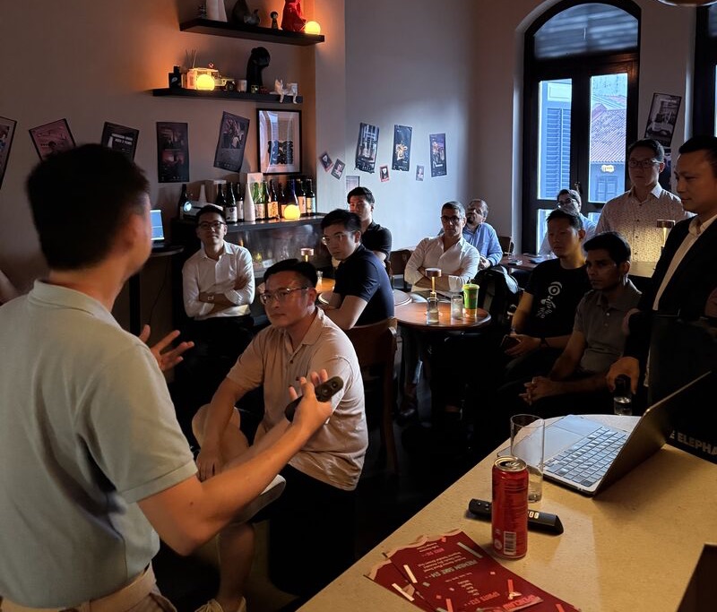 Speaker gesturing to a small audience beside an open laptop